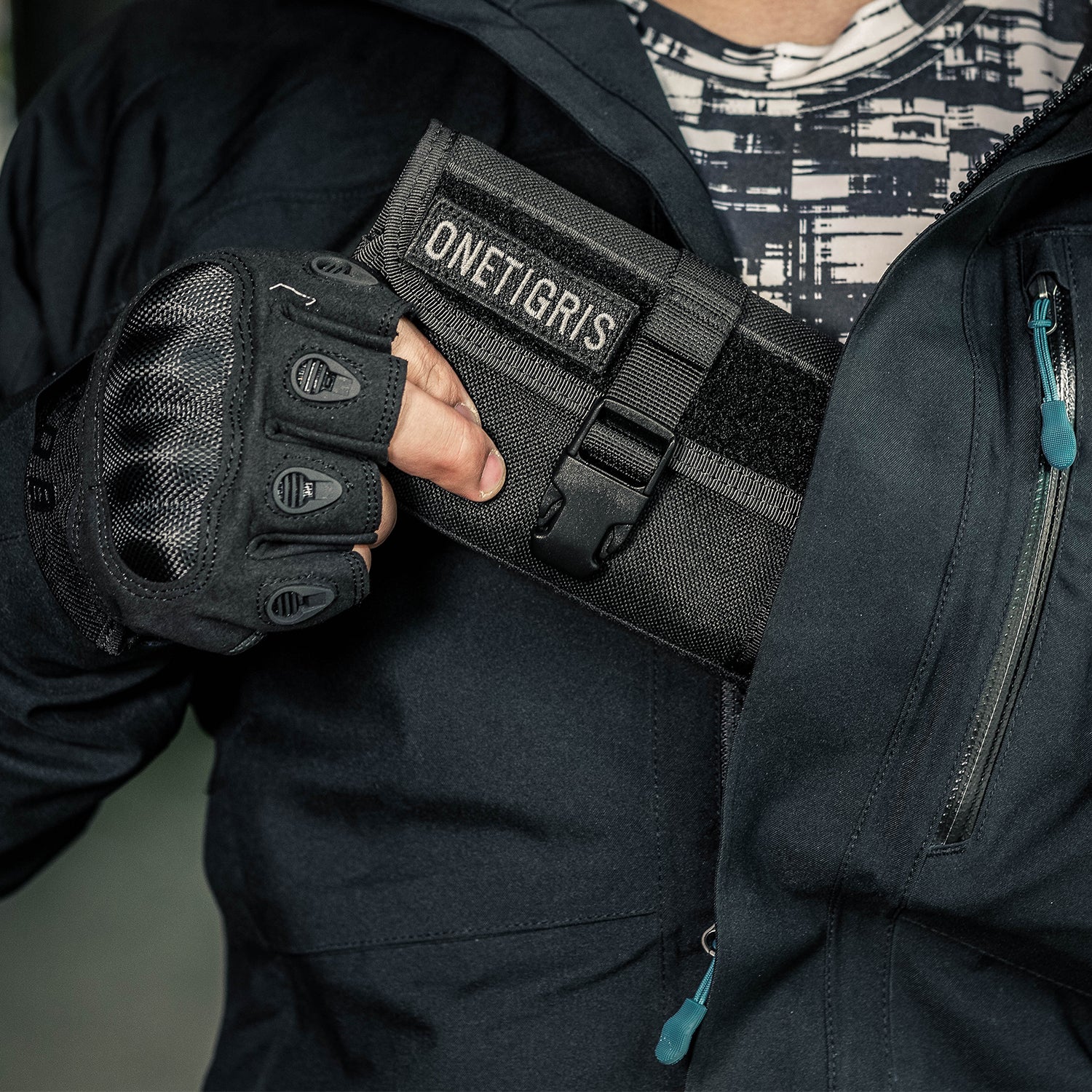 Person wearing tactical gloves with 'ONETIGRIS' branding, holding a black bag.